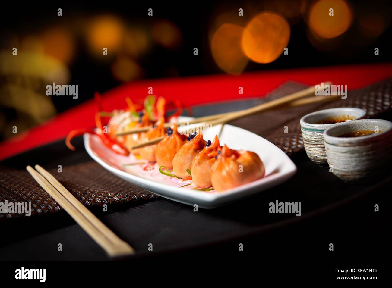 Un piatto gourmet di vivaci gnocchi al vapore conditi con guarnigione, serviti con salse a base di soia. Su un elegante tavolo con bacchette, perfetto per Foto Stock