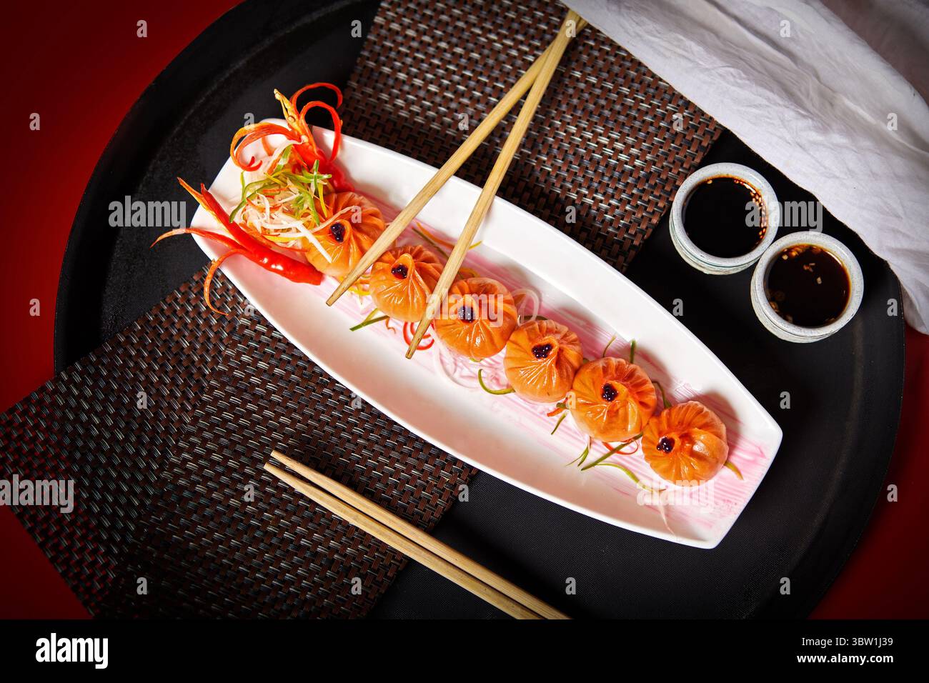 Una fila splendidamente placcata di gnocchi gourmet guarniti con peperoncino e verdure, serviti con salsa di soia e bacchette. Una vista dall'alto verso il basso dell'autentica Asia Foto Stock