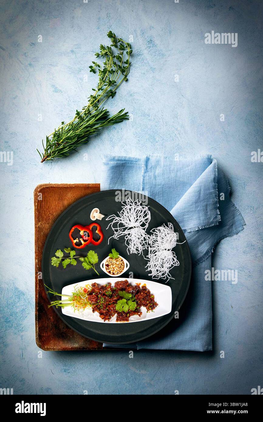 Un piatto di pollo croccante splendidamente placcato con spaghetti fritti, erbe, peperoni e arachidi tritate. Una miscela gourmet di sapori e consistenze, in stile Foto Stock