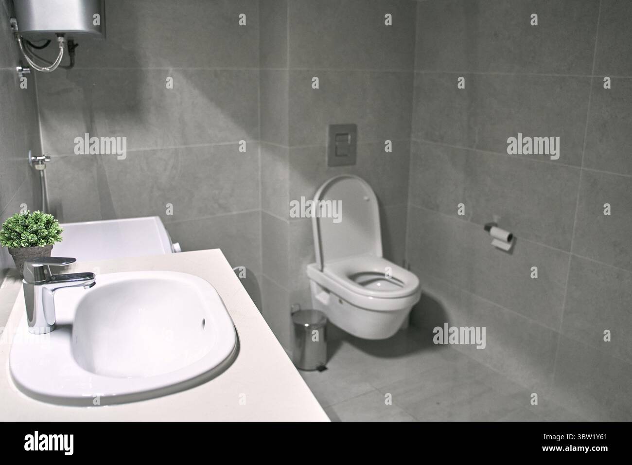 Un bagno moderno con WC a parete e lavandino, progettato con un'estetica minimalista e pulita. lo spazio è rivestito di piastrelle, sottolineando fu Foto Stock