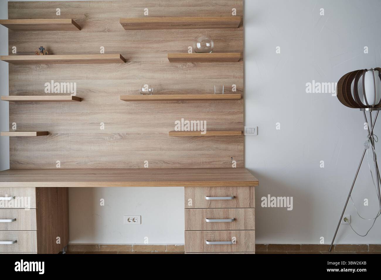 Uno spazio di lavoro minimalista con una scrivania in legno con ripiani galleggianti e una lampada da terra moderna, ideale per un design elegante e organizzato degli interni. Foto Stock