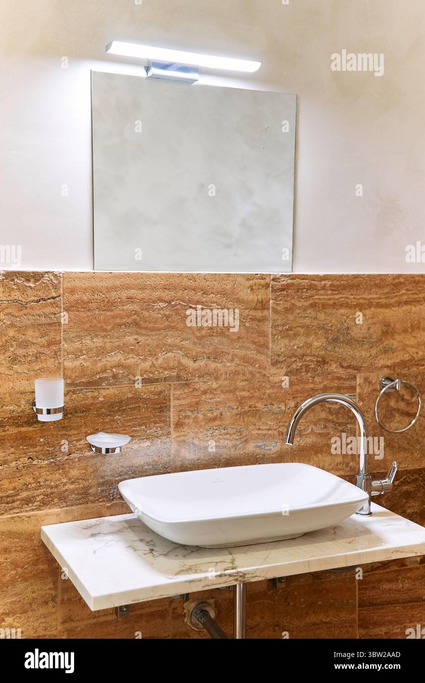 Un bagno contemporaneo con lavandino in marmo pulito, finiture eleganti e un decor elegante, impreziosito da luci soffuse e uno specchio riflettente per un lu Foto Stock