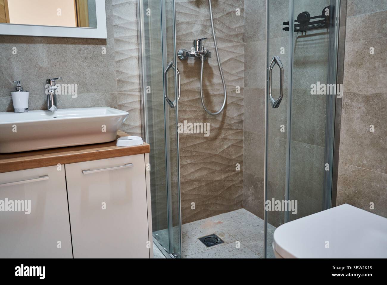 Bagno moderno con doccia in vetro, elegante lavello bianco, lavandino con finiture in legno e piastrelle eleganti per un look elegante e moderno. Foto Stock