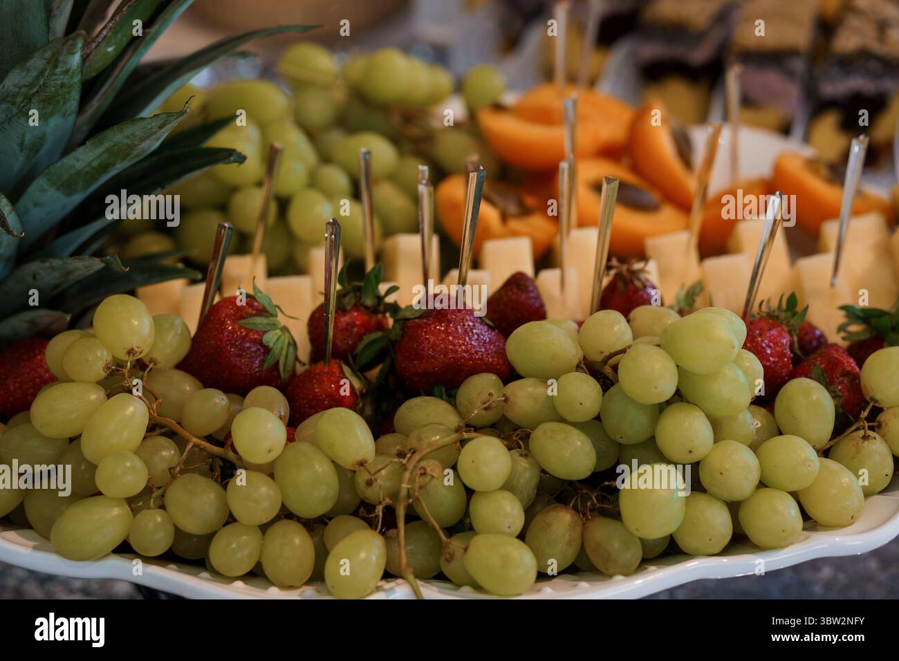 Uno shot ravvicinato mostra un piatto di frutta ben organizzato con uva verde fresca, fragole mature, una fetta di ananas, cantaloupe e formaggi Foto Stock