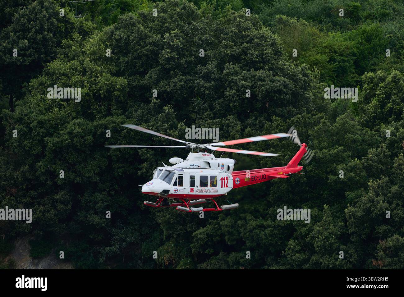 Elicottero di soccorso rosso e bianco che sorvola una lussureggiante foresta verde, fornendo servizi di emergenza e assistenza Foto Stock