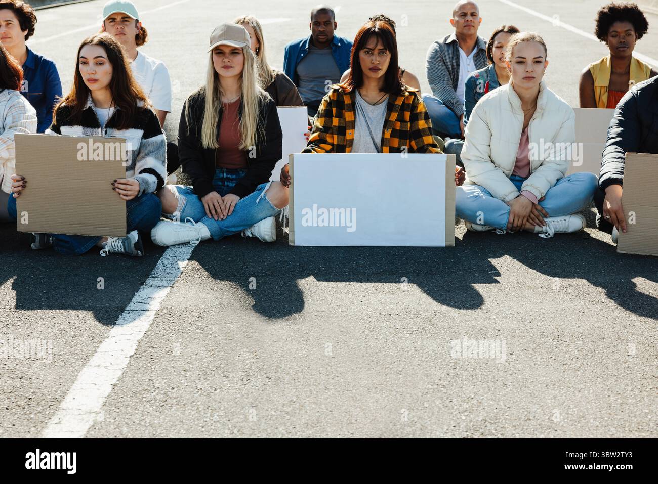 Un gruppo di giovani adulti seduti con cartelli bianchi, che partecipano a una manifestazione pacifica, simboleggiando la loro solidarietà e attivismo per la pubblicità Foto Stock