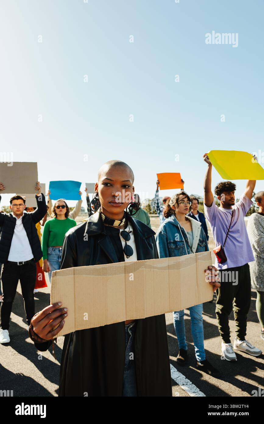 Una giovane donna è in prima linea in una protesta, tenendo un cartello di cartone vuoto con un comportamento espressivo. Un gruppo eterogeneo di persone che detengono muli Foto Stock