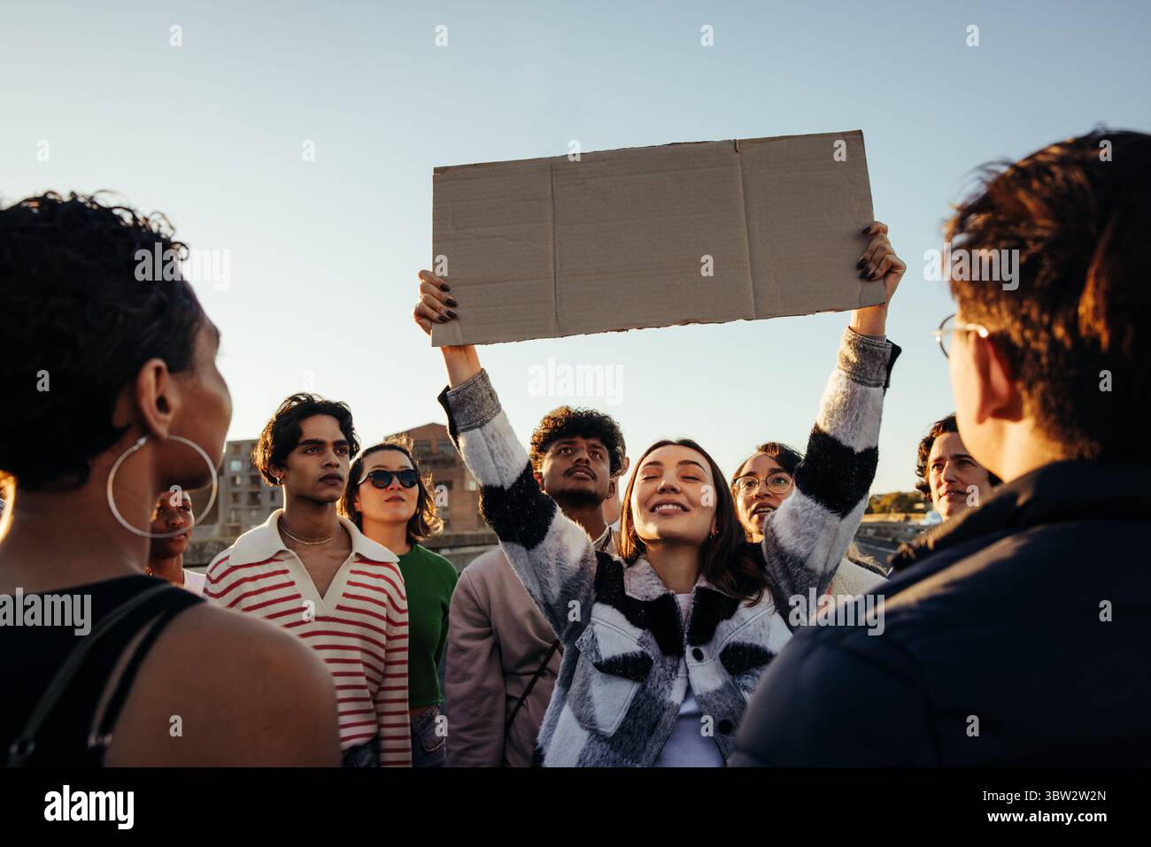 Un gruppo di diversi giovani adulti si è riunito durante una protesta, con uno che tiene un cartello di cartone mentre altri mostrano un'attesa attenta e determinata Foto Stock