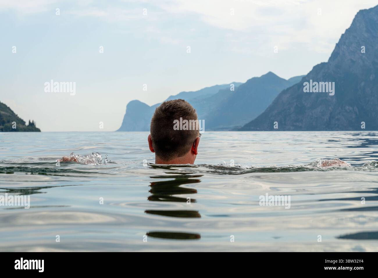 Torbole, Lago di Garda, Italia - 15 luglio 2025: Un uomo nuota da solo nell'ampia distesa del Lago di Garda - superficie calma, ma rischi invisibili. Immagine simbolica dei pericoli sottostimati per la balneazione, dell'annegamento e della mancanza di supervisione in acque aperte. *** Ein Mann schwimmt allein im weiten Gardasee stille Oberfläche, aber unsichtbare Risiken. Symbolbild für unterschätzte Badegefahren, Ertrinken und fehlende Aufsicht im offenen Gewässer. Foto Stock