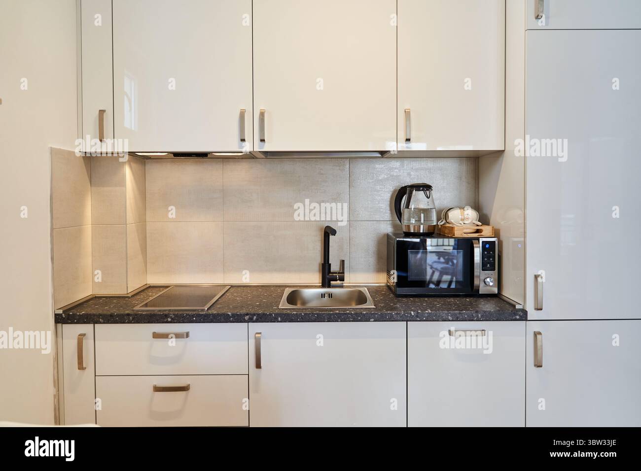 Una cucina moderna con armadi bianchi e un elegante ripiano nero, completo di elettrodomestici essenziali come un microonde e un bollitore. perfetto per Foto Stock