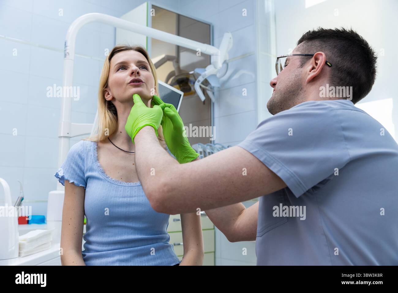 Una giovane donna e un dentista in un ambiente clinico, impegnandosi in un attento esame delle caratteristiche del viso con attenzione focalizzata per la salute ottimale e Foto Stock