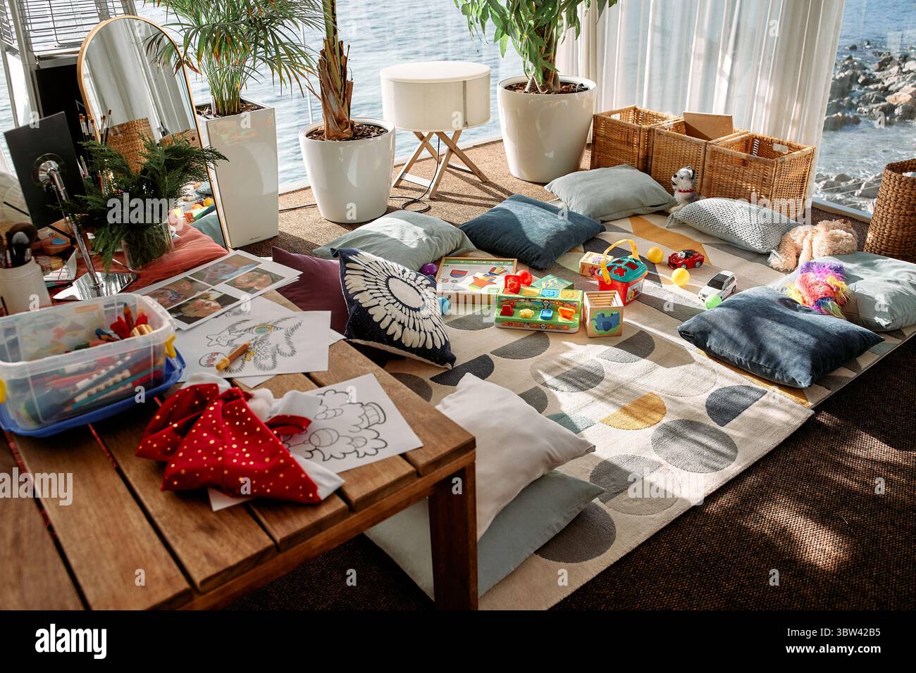Un'accogliente sala giochi per bambini con una splendida vista sull'oceano, dotata di cuscini, giocattoli, oggetti d'arte e piante, offre un ambiente perfetto per la creatività e la creatività Foto Stock