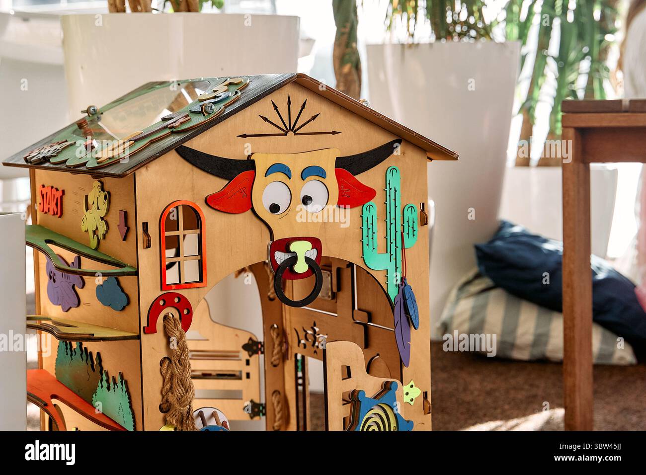 Una colorata casa di gioco in legno con il volto di un toro e elementi interattivi offre ai bambini un'esperienza di gioco creativa e istruttiva in un ambiente vivace Foto Stock