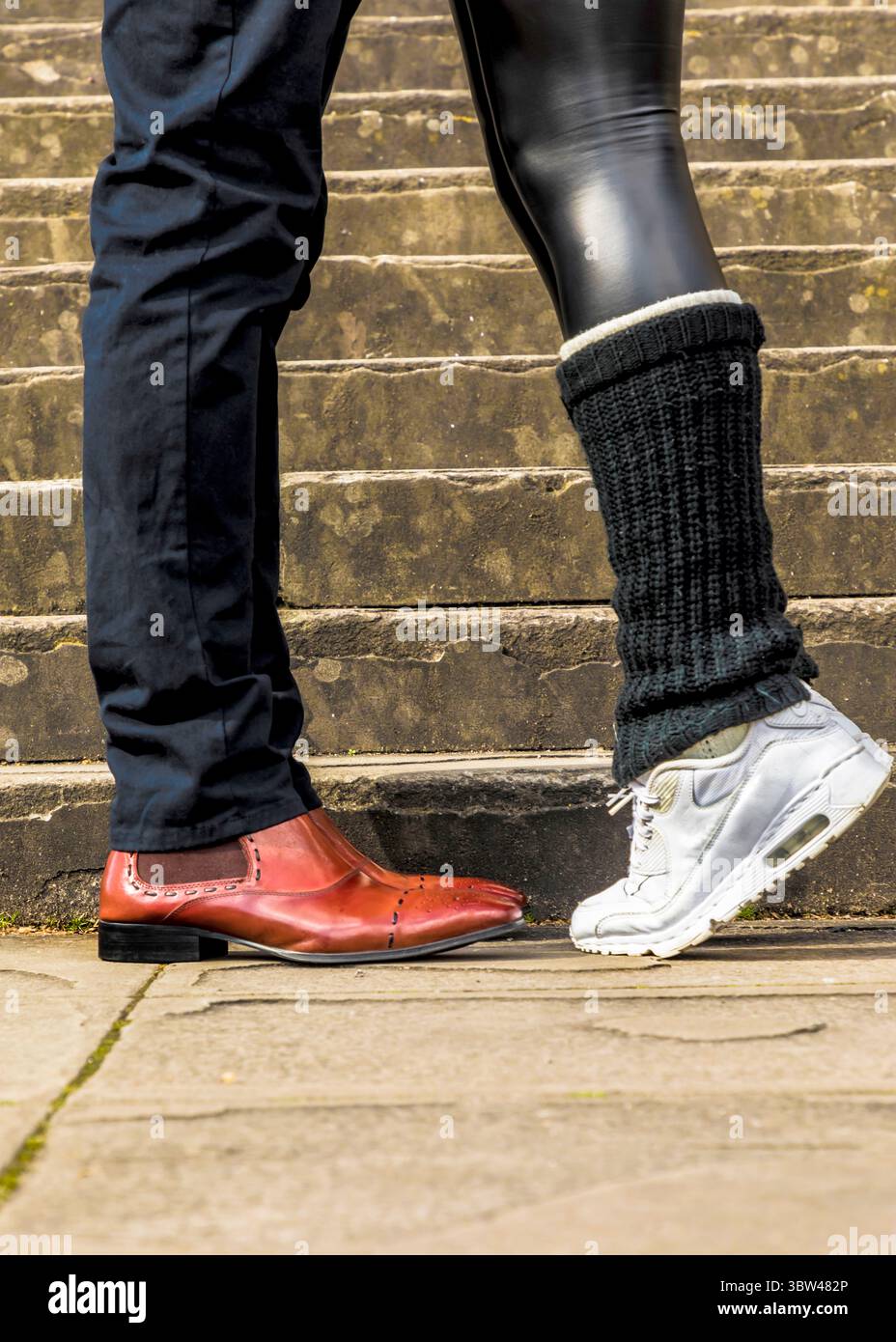 Un uomo con scarpe da passeggio si trova accanto a una persona che indossa scarpe da ginnastica e scalda gambe. Foto Stock