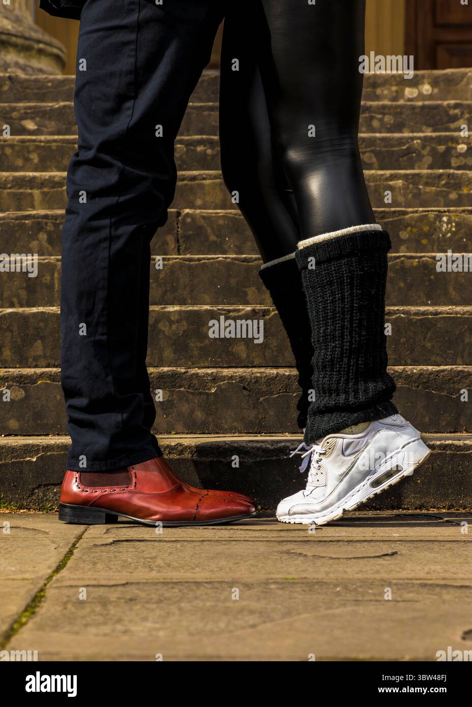 Un uomo con scarpe in pelle rossa si trova accanto a una persona che indossa scarpe da ginnastica bianche e leggings neri. Foto Stock