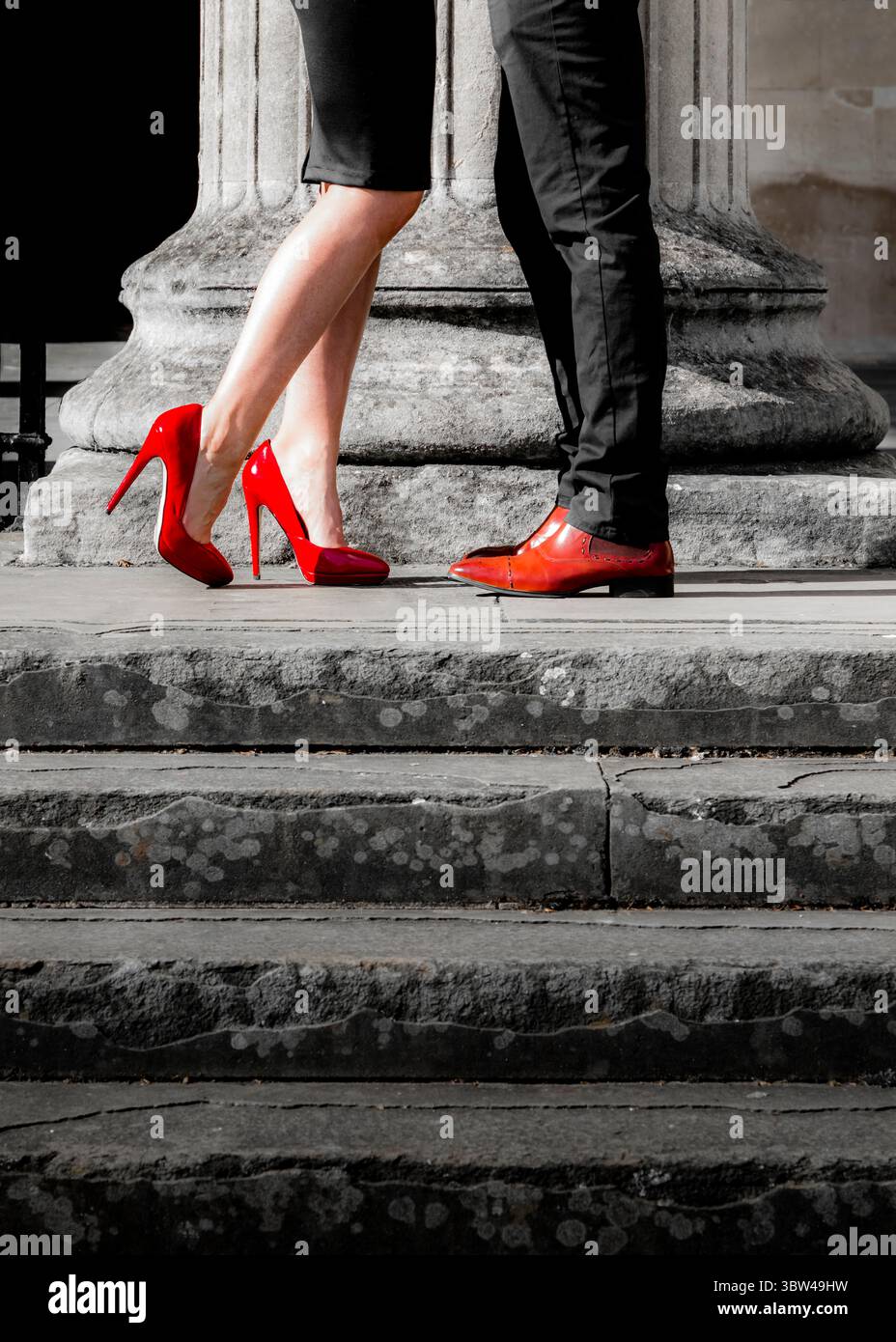 Una donna con gonna nera e tacchi alti rossi si erge su una serie di gradini di pietra, di fronte a un uomo con pantaloni neri e scarpe rosse. Foto Stock