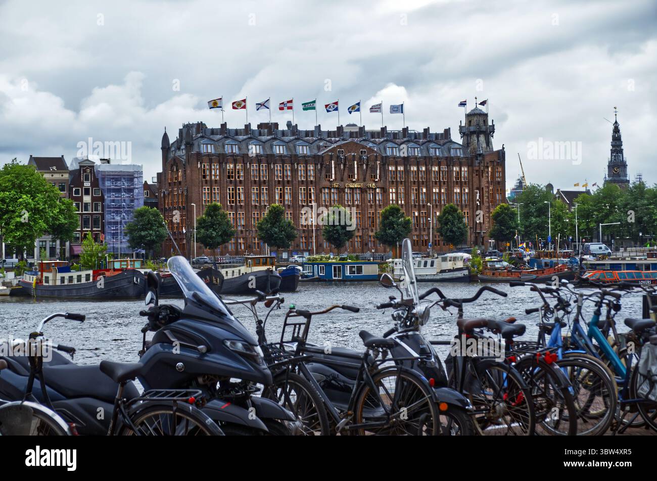 Biciclette appoggiate su edifici storici sul lungofiume, catturando il paesaggio urbano iconico di amsterdam e la cultura ciclistica lungo il fiume amstel Foto Stock