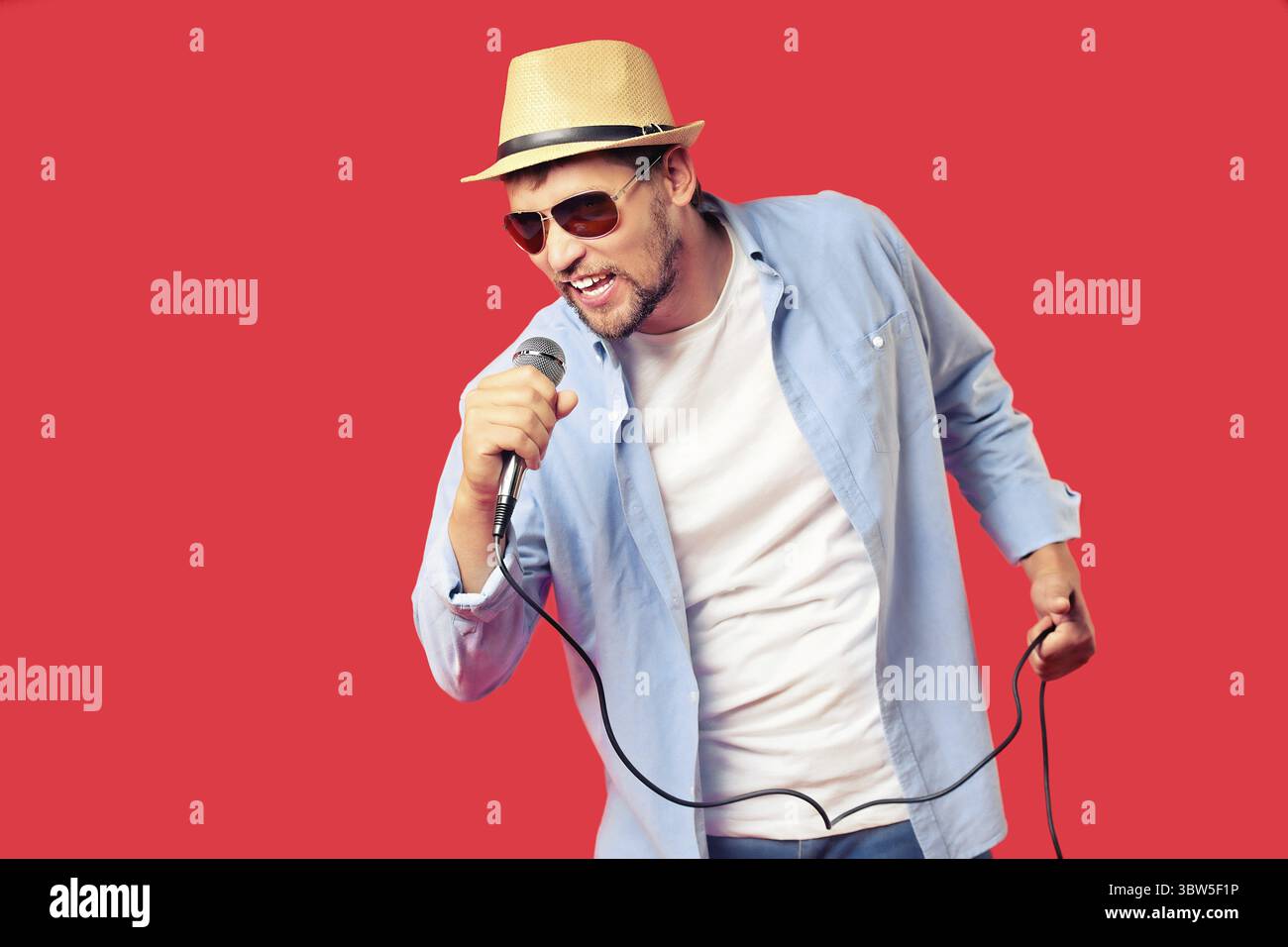 Un uomo bianco in un cappello e occhiali da sole canta una canzone in un microfono. Esecuzione vocale della canzone. Sfondo pubblicitario per un karaoke club o bar. R Foto Stock