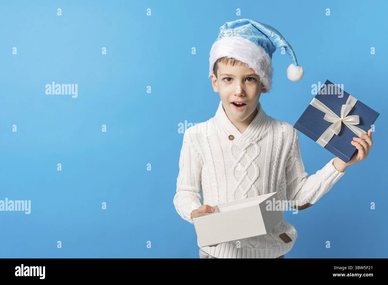 Gluecklicher kleiner Junge in Blauen Weihnachtshut mit einem Geschenk-Box Kopierraum. Leerer Platz fuer ihren Text. Winterferien und aktuelles Konzept Foto Stock