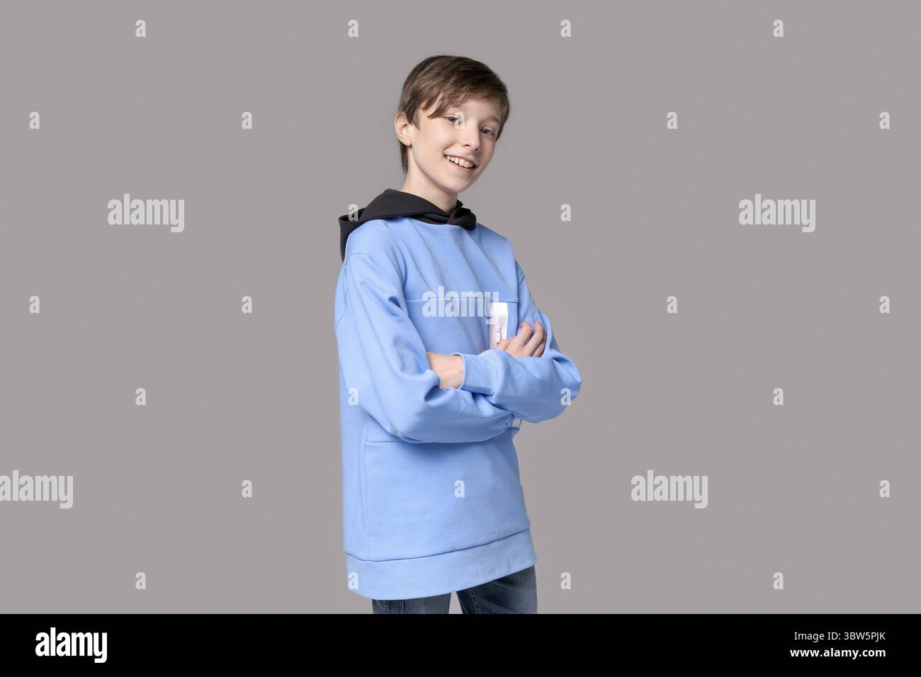Ritratto uomo felice caucasico adolescente in felpa blu su sfondo grigio. Allegro modello maschile caucasico sorridente con un sorriso bianco in stile Foto Stock