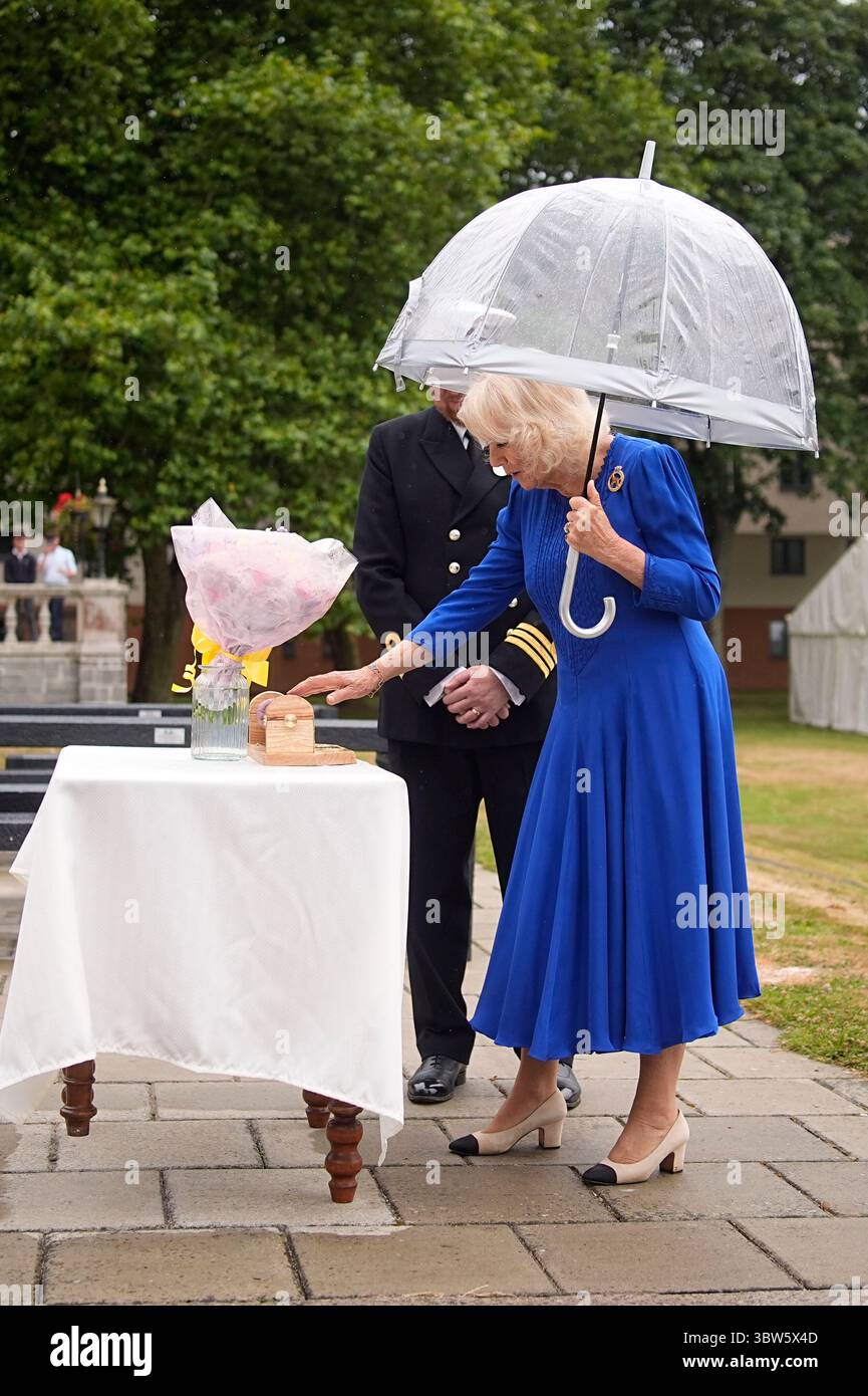 La regina Camilla viene presentata con fiori e un portarotolo di pellicola trasparente durante una festa in giardino per la HMS Astute Ship Company e le loro famiglie a HMS Drake, HMNB Devonport a Plymouth, Devon, per segnare la fine della prima commissione del sottomarino Astute, che è la prima commissione più lunga di qualsiasi sottomarino della Royal Navy nella storia, con oltre 15 anni. Data foto: Mercoledì 16 luglio 2025. Foto Stock