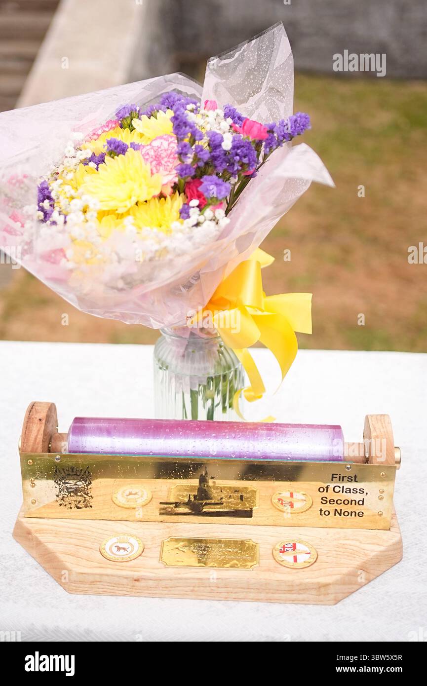 Fiori e un portarotolo di pellicola trasparente che è stato presentato alla regina Camilla durante una festa in giardino per la HMS Astute Ship Company e le loro famiglie a HMS Drake, HMNB Devonport a Plymouth, Devon, per segnare la fine della prima commissione del sottomarino Astute, che è la prima commissione più lunga di qualsiasi sottomarino della Royal Navy nella storia, con oltre 15 anni. Data foto: Mercoledì 16 luglio 2025. Foto Stock