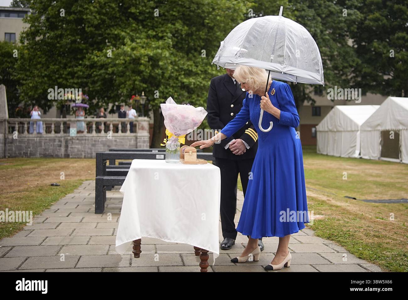 La regina Camilla viene presentata con fiori e un portarotolo di pellicola trasparente durante una festa in giardino per la HMS Astute Ship Company e le loro famiglie a HMS Drake, HMNB Devonport a Plymouth, Devon, per segnare la fine della prima commissione del sottomarino Astute, che è la prima commissione più lunga di qualsiasi sottomarino della Royal Navy nella storia, con oltre 15 anni. Data foto: Mercoledì 16 luglio 2025. Foto Stock