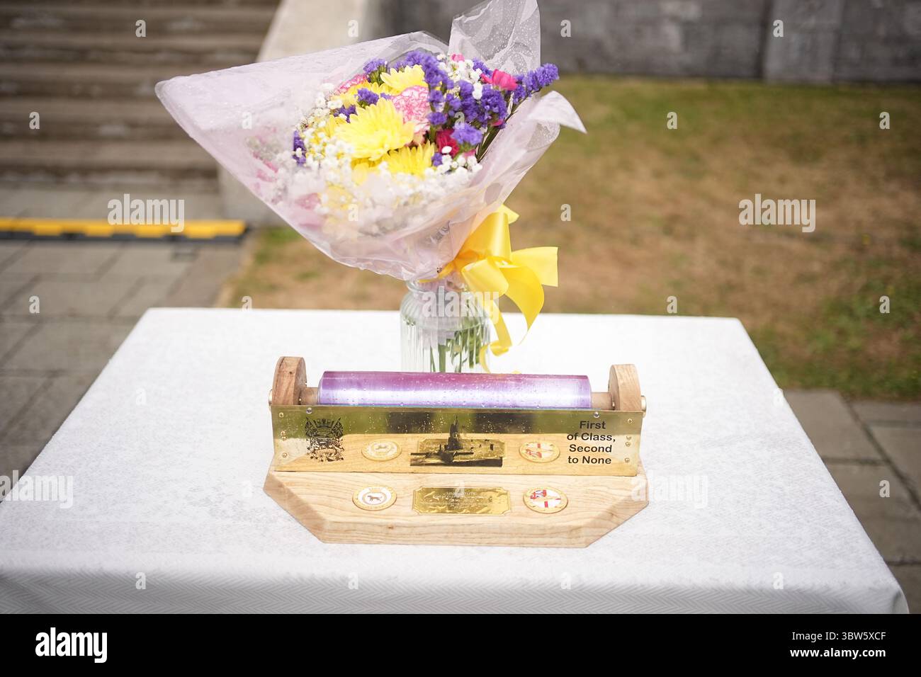 Fiori e un portarotolo di pellicola trasparente che è stato presentato alla regina Camilla durante una festa in giardino per la HMS Astute Ship Company e le loro famiglie a HMS Drake, HMNB Devonport a Plymouth, Devon, per segnare la fine della prima commissione del sottomarino Astute, che è la prima commissione più lunga di qualsiasi sottomarino della Royal Navy nella storia, con oltre 15 anni. Data foto: Mercoledì 16 luglio 2025. Foto Stock