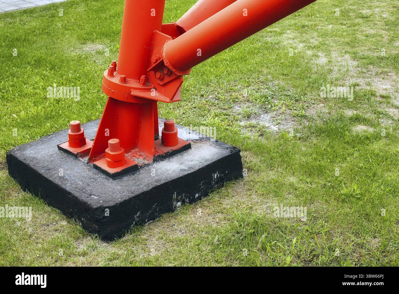 Si tratta di un supporto o di un palo in metallo rosso fissato alla base in calcestruzzo con grandi bulloni e dadi di ancoraggio. Struttura affidabile e stabile. Sfondo o sc Foto Stock
