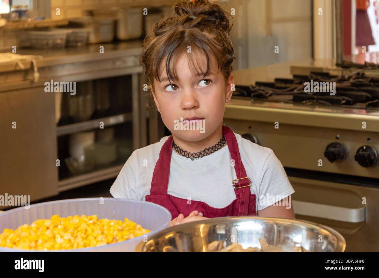 Un bambino in una cucina professionale è coinvolto nella cucina, mostrando un interesse per la preparazione del cibo Foto Stock