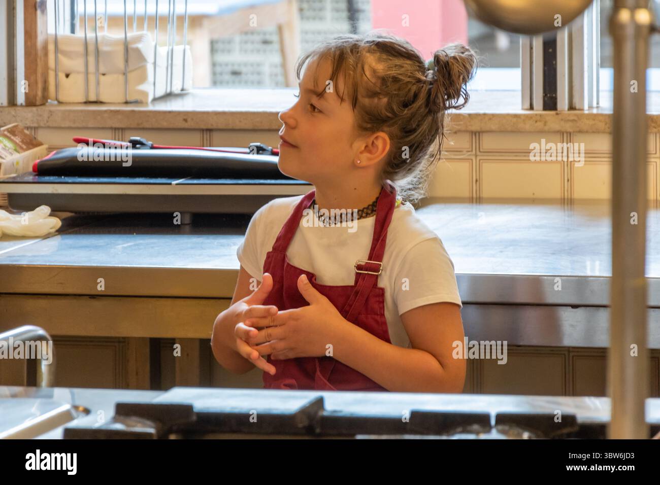 Una ragazza con una maglietta bianca e un grembiule Bordeaux aiuta in cucina. Foto Stock