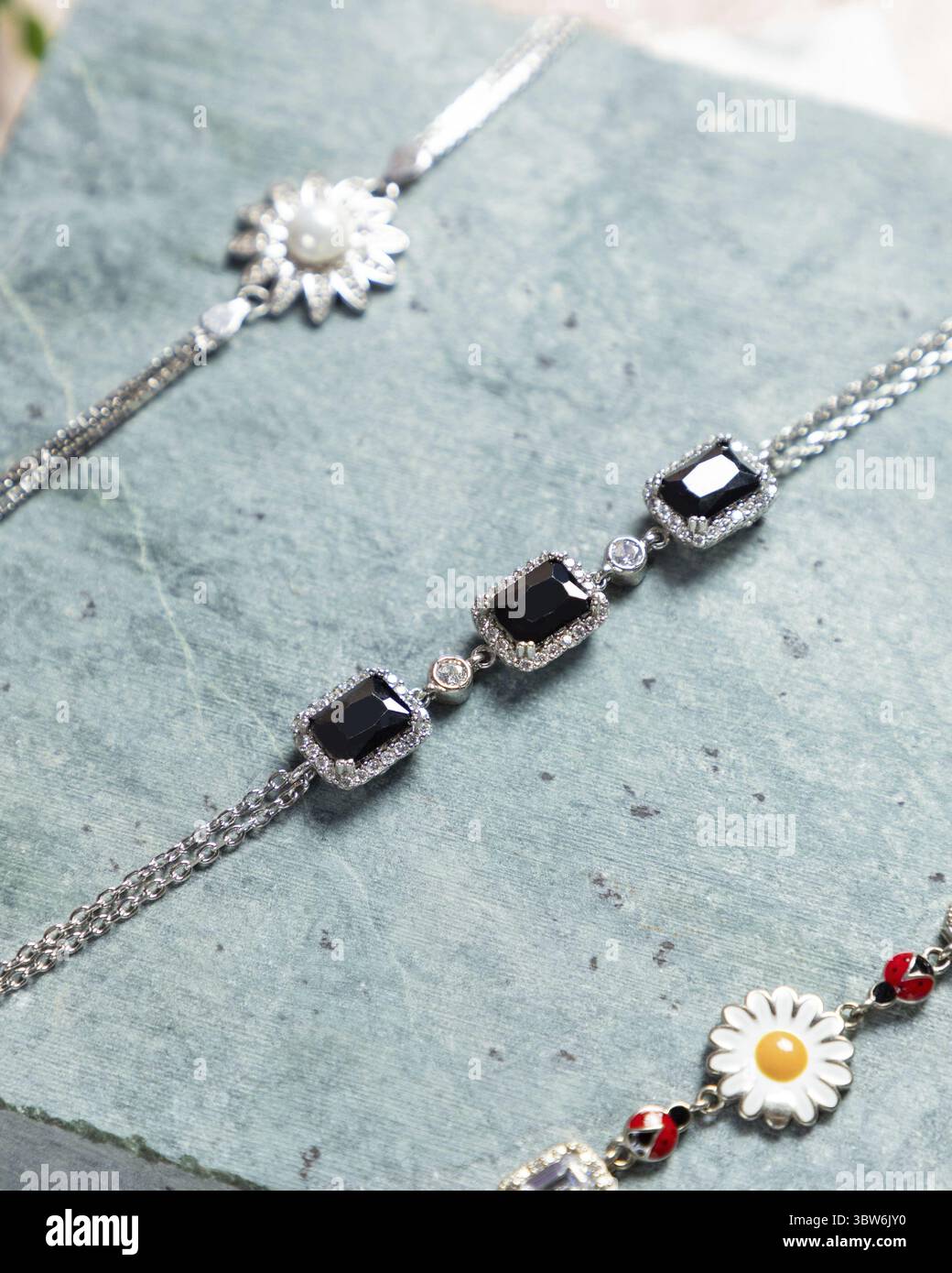 Tre braccialetti con pietre preziose nere e diamanti sono adagiati su una superficie di pietra Foto Stock