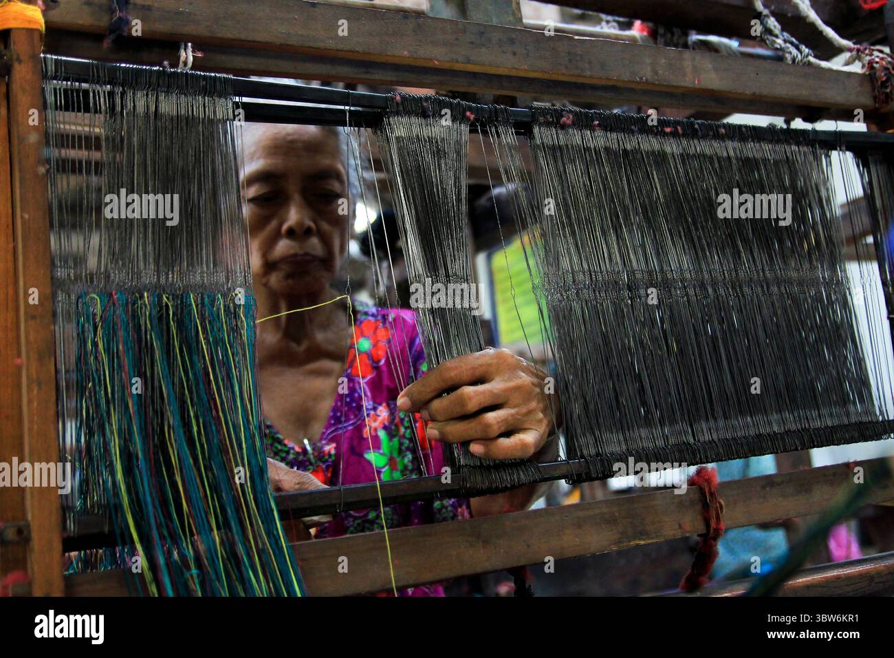 Un anziano artigiano prepara un telaio tradizionale prima di iniziare il suo lavoro in una fabbrica tessile. Foto Stock