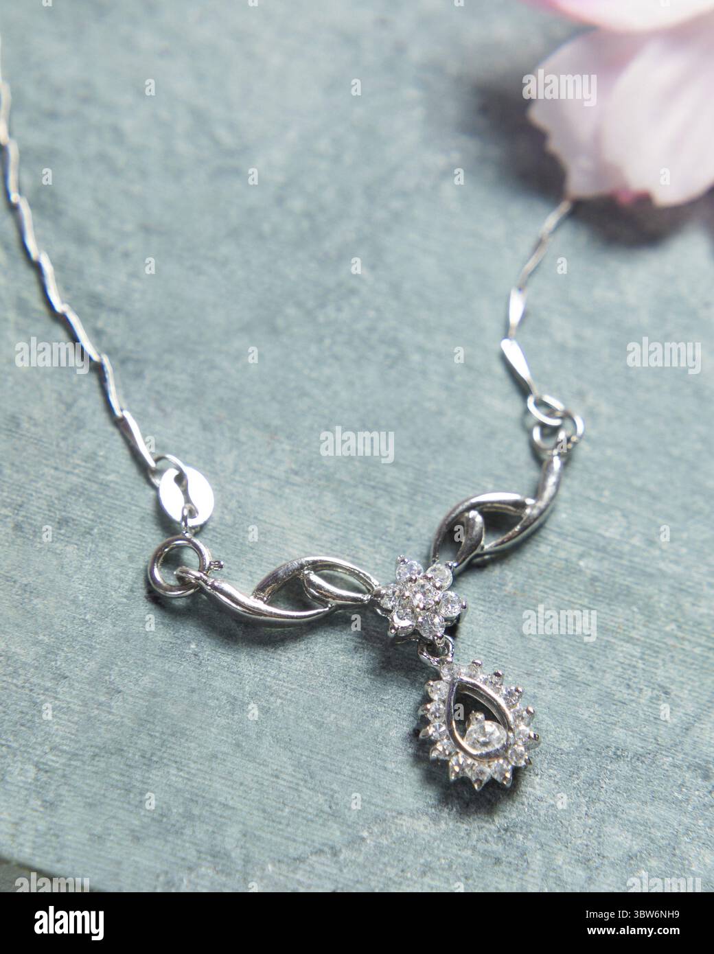 Elegante collana in argento con diamanti su sfondo blu decorata con petali di fiori Foto Stock