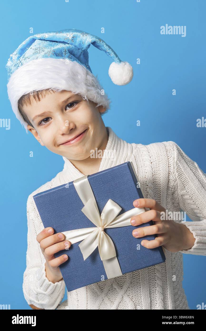 Gluecklicher kleiner Junge in Blauen Weihnachtshut mit einem Geschenk-Box Kopierraum. Leerer Platz fuer ihren Text. Winterferien und aktuelles Konzept Foto Stock