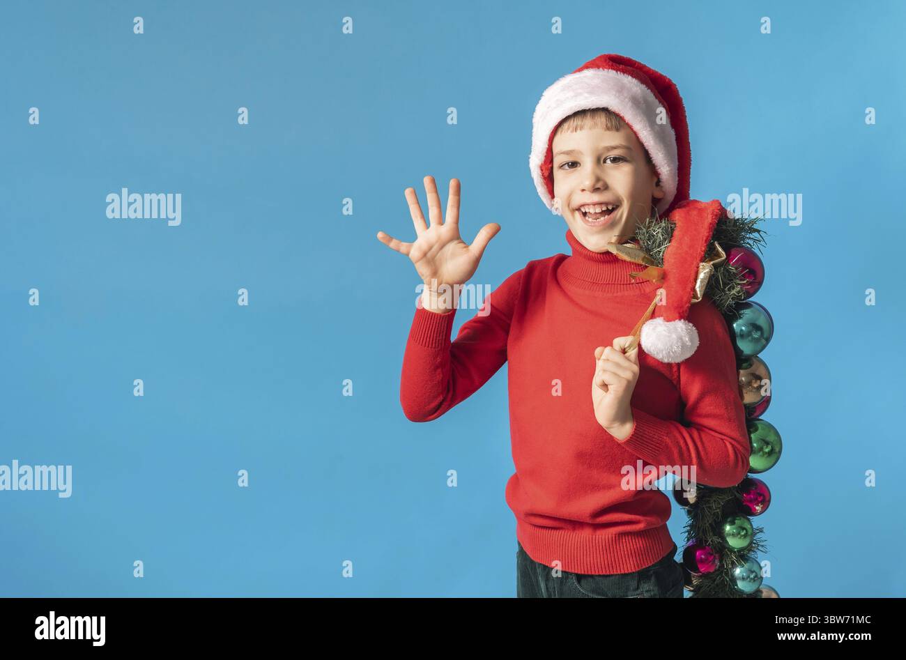 Froehliches Kind in Santa Hut halten Weihnachten dekorative Kugeln auf blauem Hintergrund, Weihnachten und Urlaub Konzept Mockup. Generazione Alpha und Foto Stock