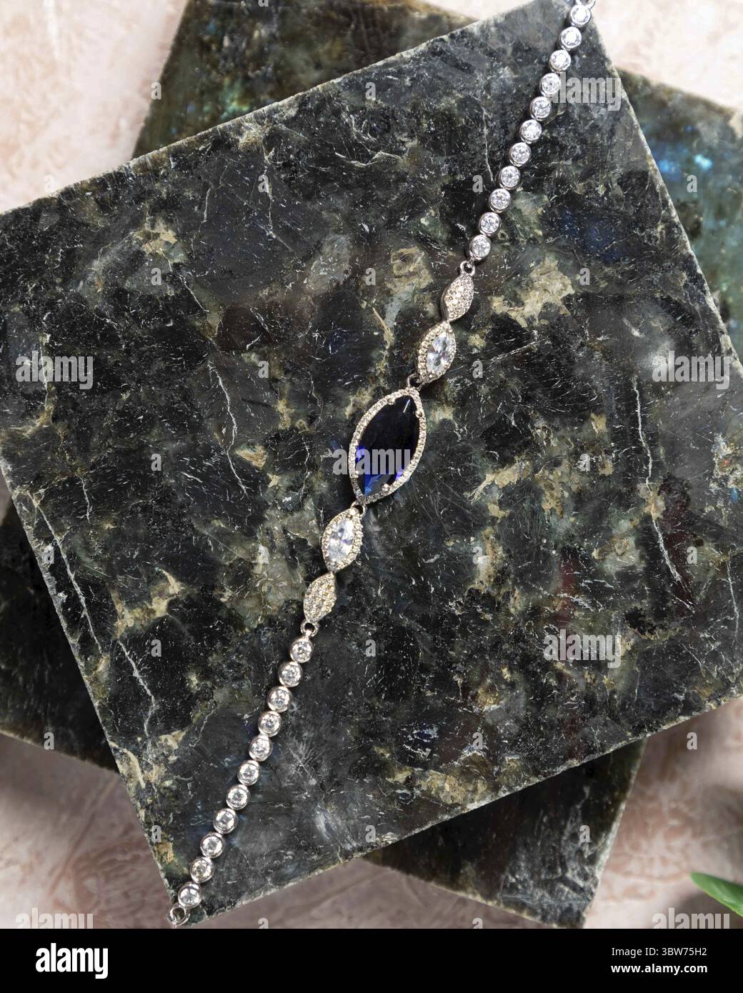 Elegante bracciale con pietre marquise blu e bianche, adagiate su una superficie di marmo scuro Foto Stock