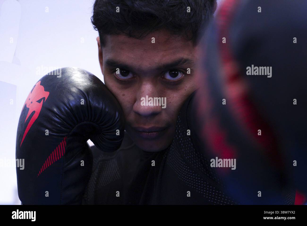 Primo piano del pugile latino con guanti neri che lanciano un allenamento di pugno nella sua palestra Foto Stock