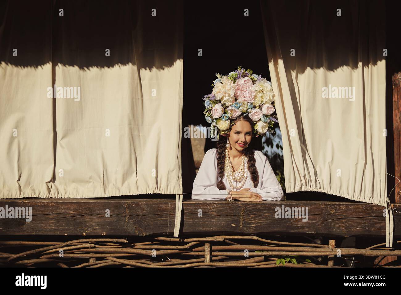 Bella donna bruna con lunghi capelli scuri, in un autentico costume nazionale ucraino bianco e una corona di fiori colorati sorride e guarda Foto Stock