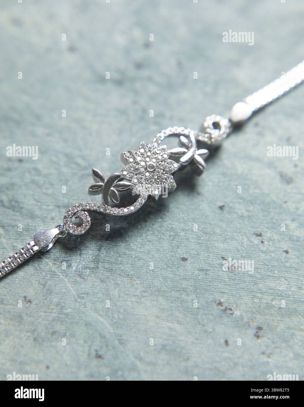 Lo splendido braccialetto con un design floreale e diamanti scintillanti si stende su una superficie blu Foto Stock