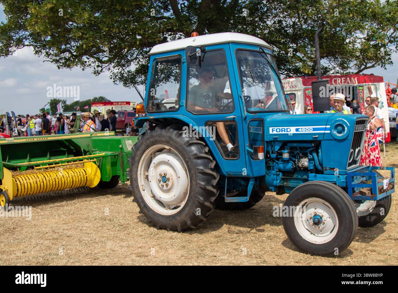 Un trattore Ford 4600 blu che tira un John Deere Bailer verde e giallo in una mostra campestre in una giornata di sole. Foto Stock