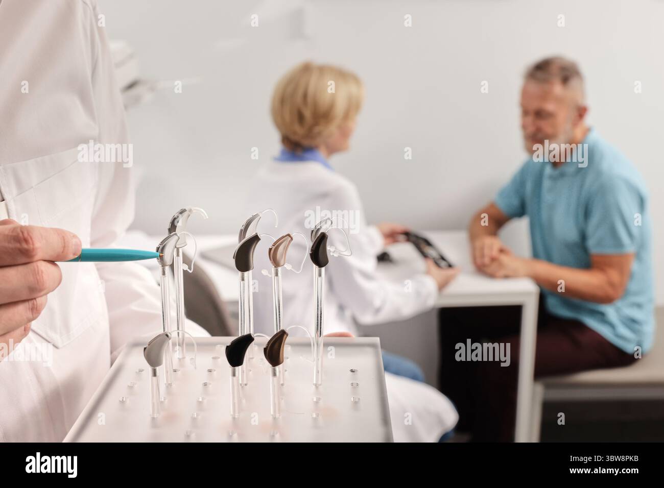 Audiologo medico che mostra il supporto con apparecchi acustici BTE di diversi tipi o colori durante la consultazione del paziente. Apparecchi acustici e soluzioni Foto Stock