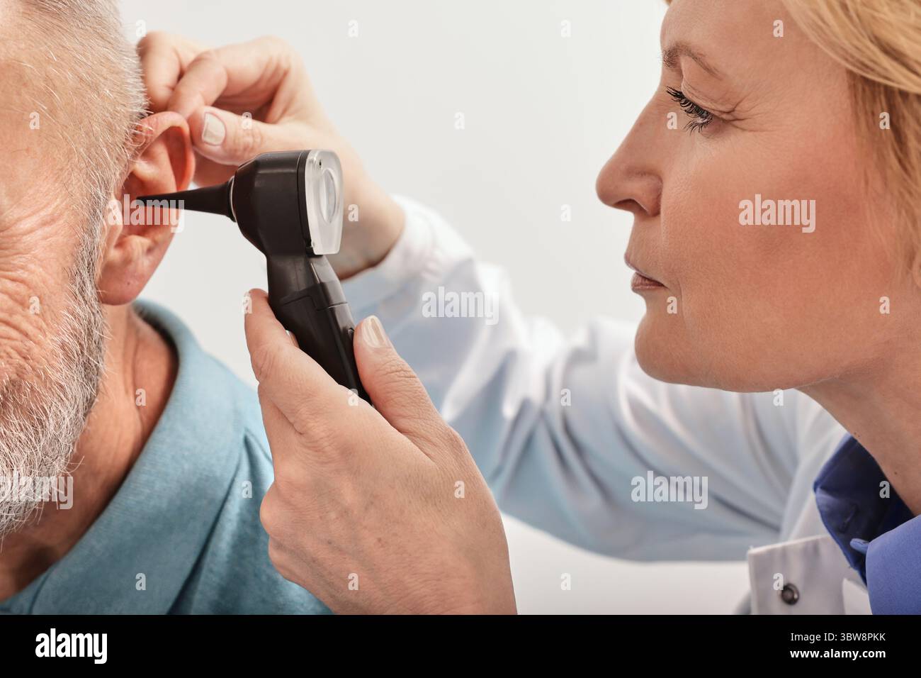 Primo piano dell'audiologo che controlla l'orecchio dell'uomo anziano con un otoscopio durante un test dell'udito in una clinica di audiologia Foto Stock