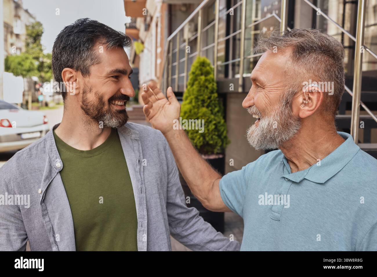 L'anziano con problemi uditivi utilizza gli apparecchi acustici per comunicare con il suo amico maschio all'aperto in città rumorosa. Soluzioni per l'udito Foto Stock