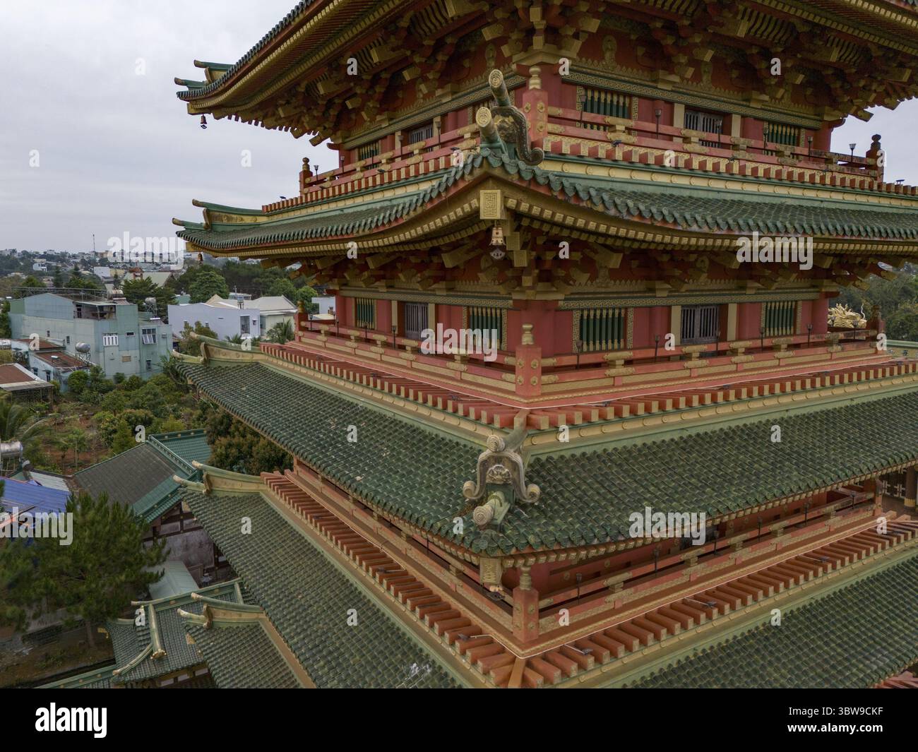 Vista aerea dell'intricata pagoda a più livelli con le sue vivaci finiture rosse e dorate che contrastano con le piastrelle verdi del tetto, Pleiku, Gia Lai, Vietnam. Foto Stock