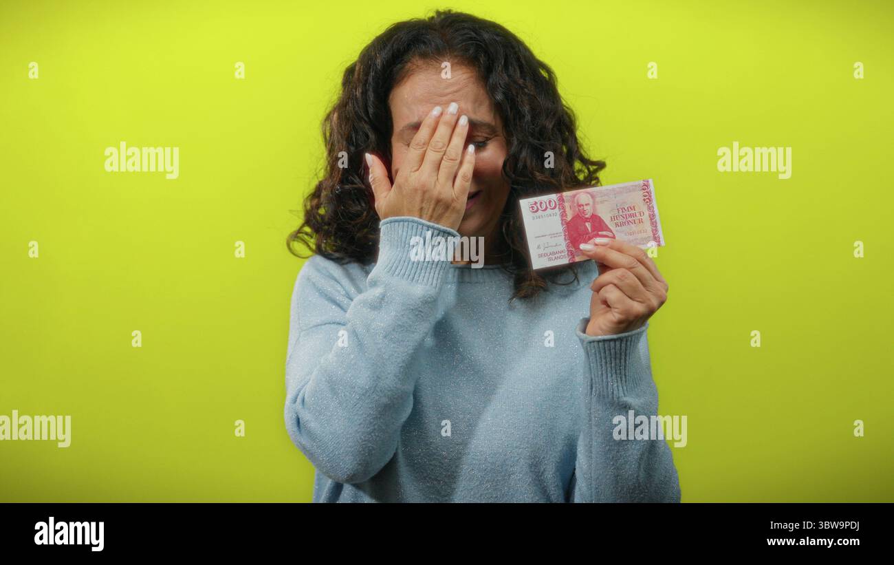 La donna che tiene in mano la corona islandese sembra preoccupata da uno sfondo giallo brillante. Foto Stock