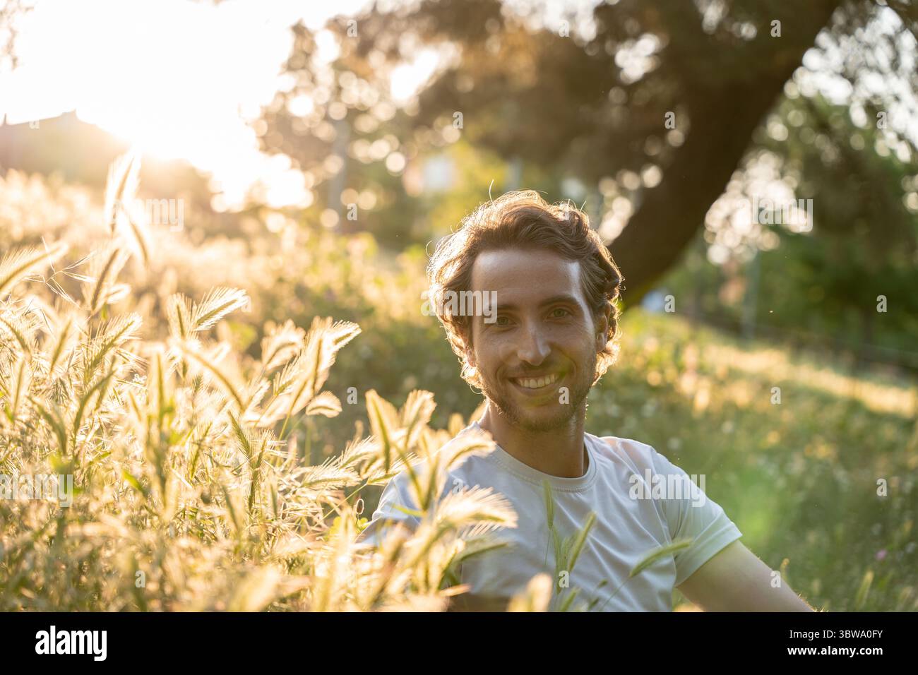 Uomo rilassato che sorride sotto la calda luce del tramonto all'aperto con un'espressione felice Foto Stock
