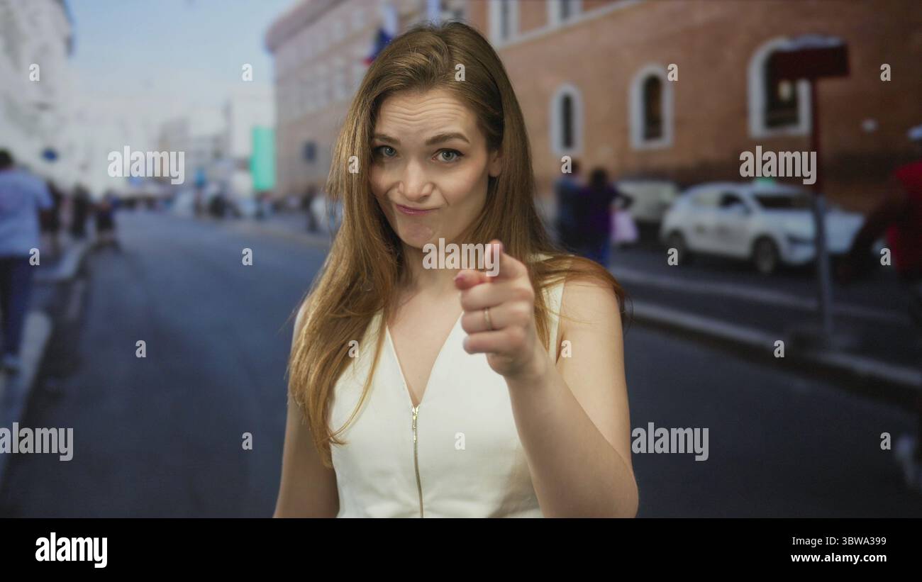 Donna che punta il dito con un feroce grimace su una strada illuminata dal sole con edifici in mattoni visibili durante il giorno; dubbio. Foto Stock