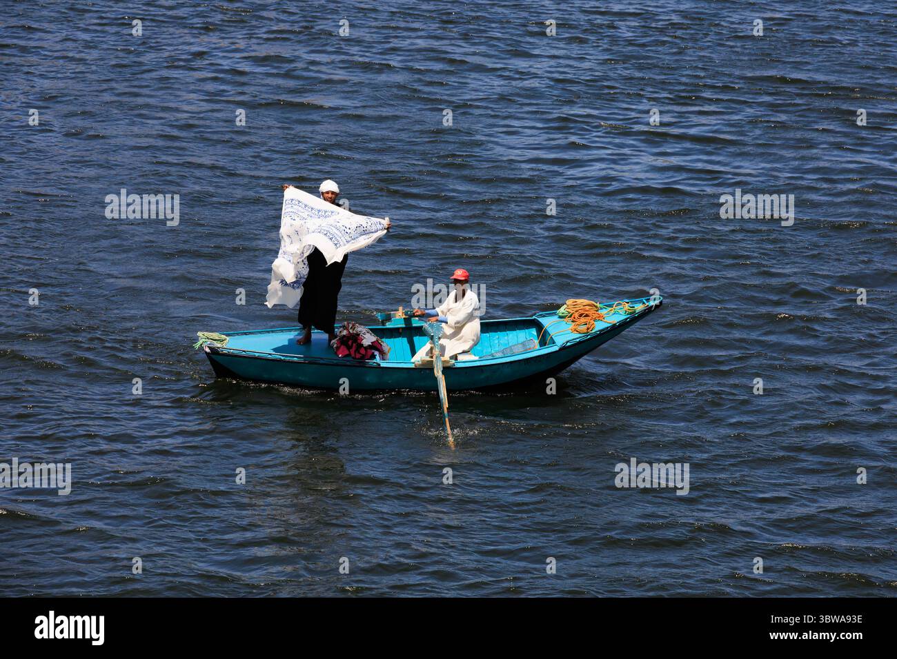 Vita quotidiana, vendendo asciugamani ai turisti di passaggio sulle navi da crociera del Nilo da una piccola barca a remi. Fiume Nilo, Egitto Foto Stock