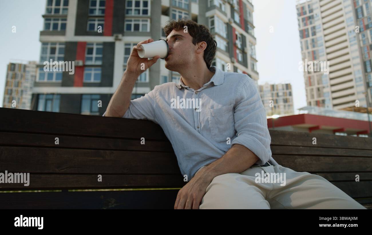 Uomo europeo caucasico seduto sulla panchina maschio che tiene tazza pausa caffè bere takeaway ordine cliente acquirente rilassarsi gustoso drink Guy studente uomo d'affari Foto Stock